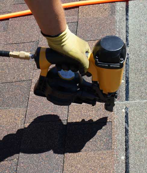 Man using a nail gun to nail down roof tiles