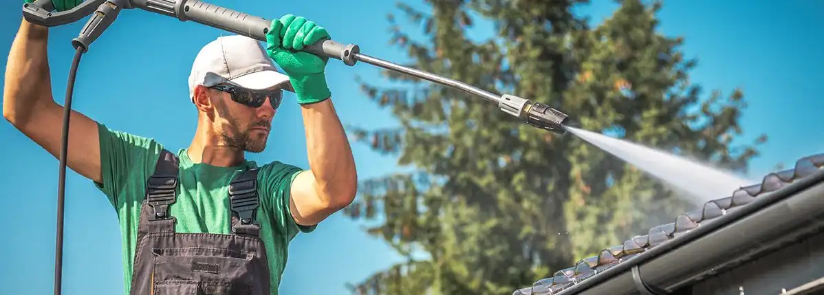 Man outside pressure washing a roof.